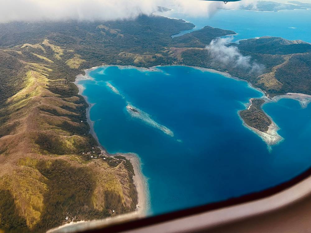 Isola verdeggiante delle Fiji circondata dal blu intenso del Pacifico, vista dal finestrino di un volo locale