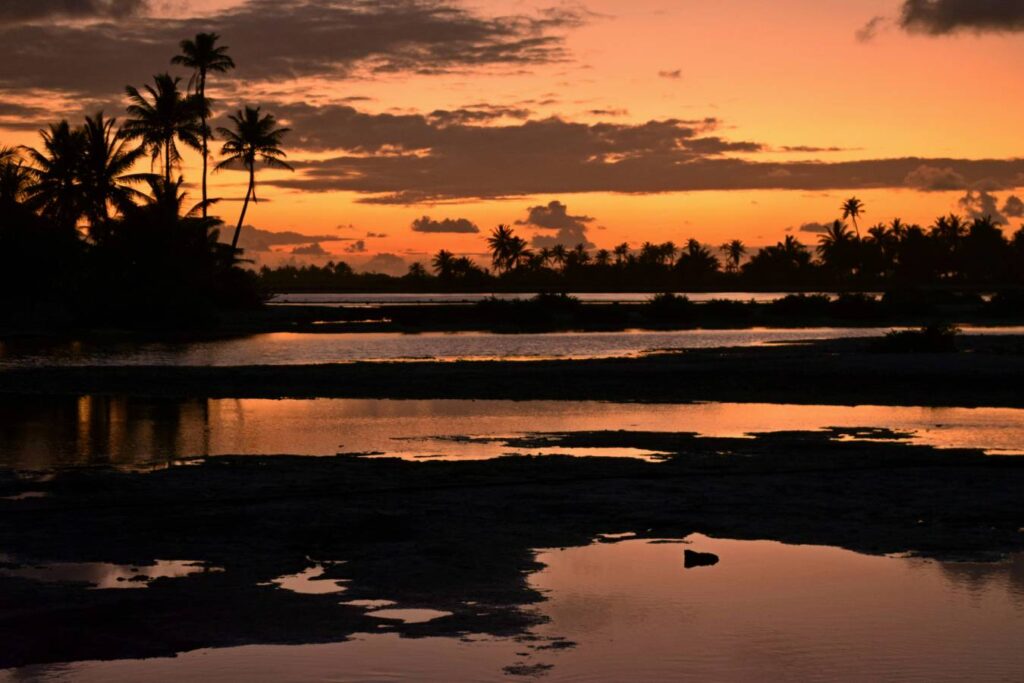 Alba sui canali naturali (“hoa”) di Tikehau che collegano diverse parti della laguna, con cielo infuocato e silhouette di palme e alberi