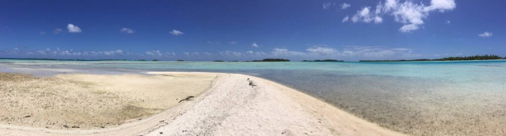Foto panoramica dalla spiaggia della Laguna Blu di Rangiroa con sabbia bianca in primo piano, mare cristallino dalle mille sfumature di azzurro e cielo azzurro limpido