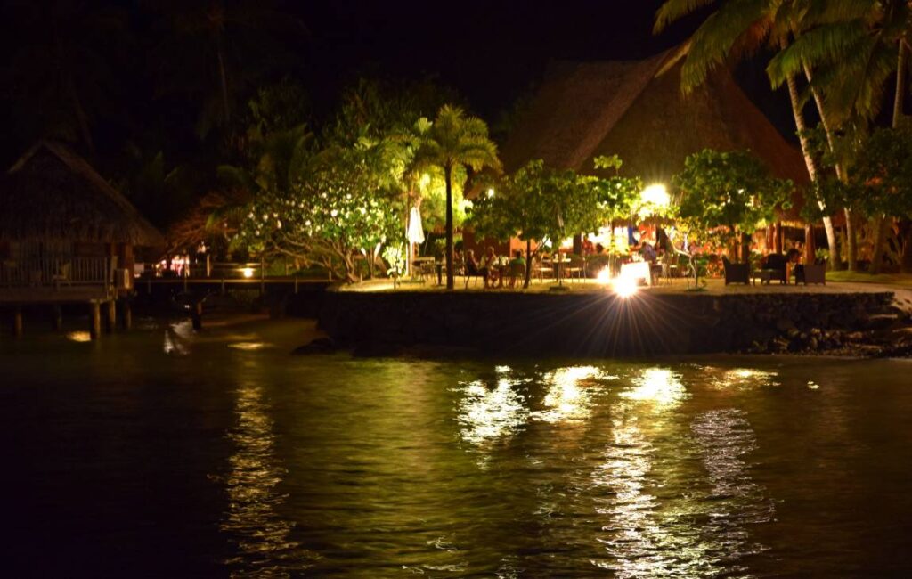 Vista notturna dal bungalow overwater sul ristorante sulla spiaggia di Bora Bora, illuminato dalle luci artificiali e affacciato sulla laguna