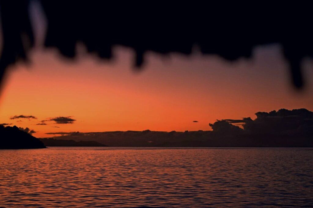 Tramonto sulla laguna di Bora Bora visto dal bungalow overwater, con le fronde del tetto del bungalow in primo piano