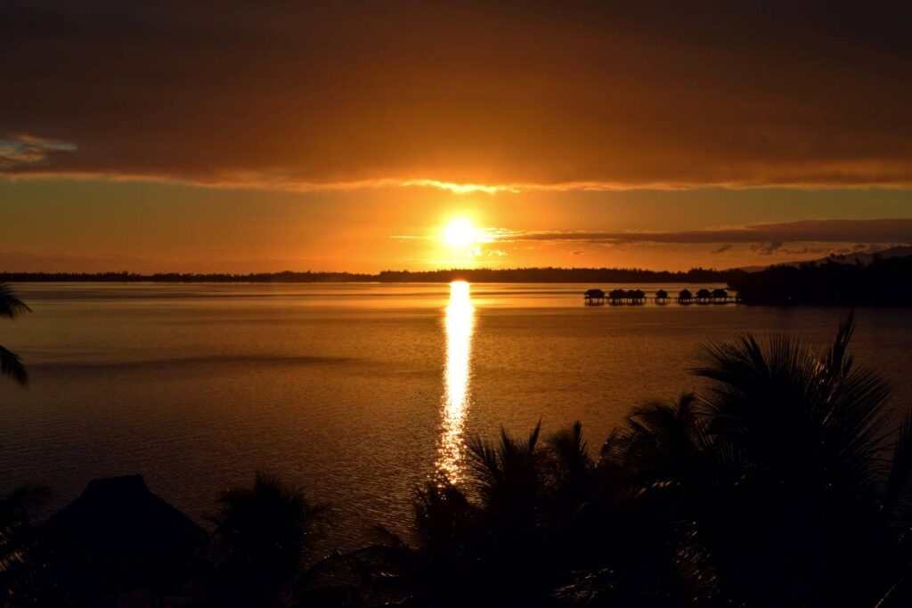 Tramonto sulla laguna di Bora Bora visto dalla camera, con il mare in primo piano, le sfumature del cielo e i bungalow overwater sullo sfondo
