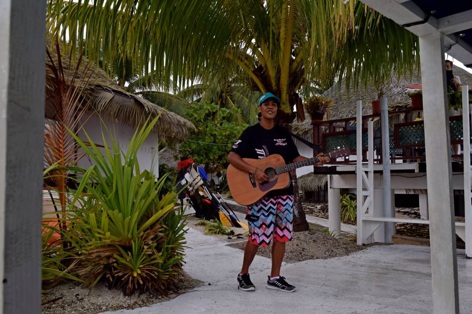 Ragazza del personale suona l’ukulele sul pontile durante il saluto di addio a Tikehau, Polinesia Francese